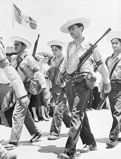 (Original Caption) Straw hatted peasant volunteers who comprised the "liberation" forces of Colonel Carlos Castillo Armas in the revolution, march back to the center of the capital after putting down an uprising by the regular Army. For the moment, at least, the regular Army Officer Corps was crushed under the weight of popular support given Col. Castillo and his irregular. The three man Junta that ruled Guatemala remained unaffected by the uprising.